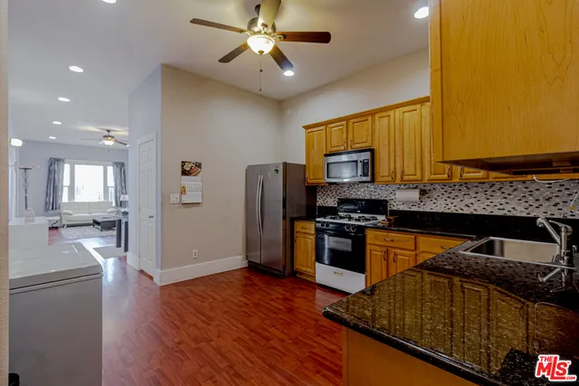 a kitchen with granite countertop a stove top oven a sink dishwasher a refrigerator and a dining table with wooden floor