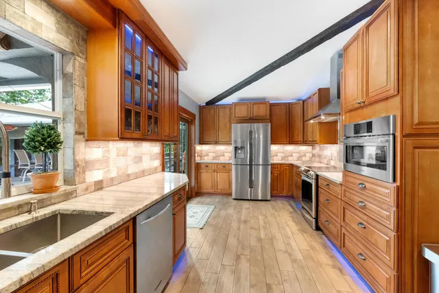 a kitchen with stainless steel appliances granite countertop a stove top oven a sink dishwasher a dining table and chairs with wooden floor