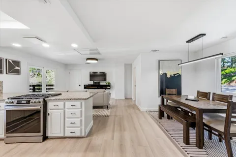 a kitchen with stainless steel appliances kitchen island granite countertop a stove top oven a sink a dining table and chairs with wooden floor