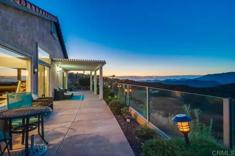 a view of a patio with dining table and chairs under an umbrella with a small yard