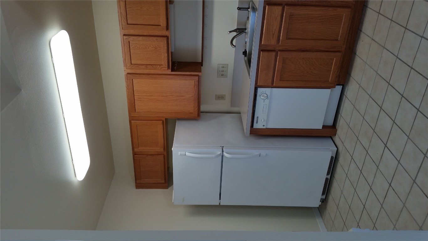 6809 West Gate Boulevard, Unit 203 Austin, TX 78745 - Photo 6 of 12 Kitchen featuring light countertops, white appliances, brown cabinetry, and light tile patterned flooring