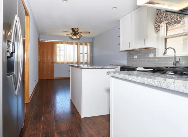 a kitchen with granite countertop a refrigerator a sink dishwasher a stove and white countertops with wooden floor