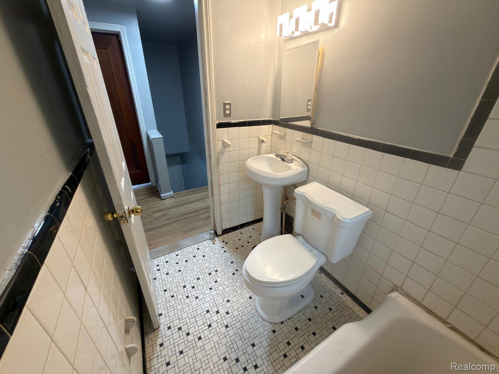 8837 Evergreen Road Detroit, MI 48228 - Photo 11 of 16 Bathroom featuring white subway tile walls with a black trim accent, a pedestal sink, a toilet, and patterned floor tiling