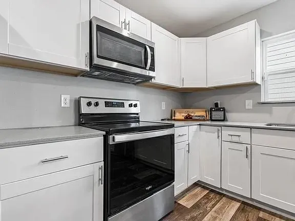a kitchen with stainless steel appliances granite countertop white cabinets a stove a microwave and a sink