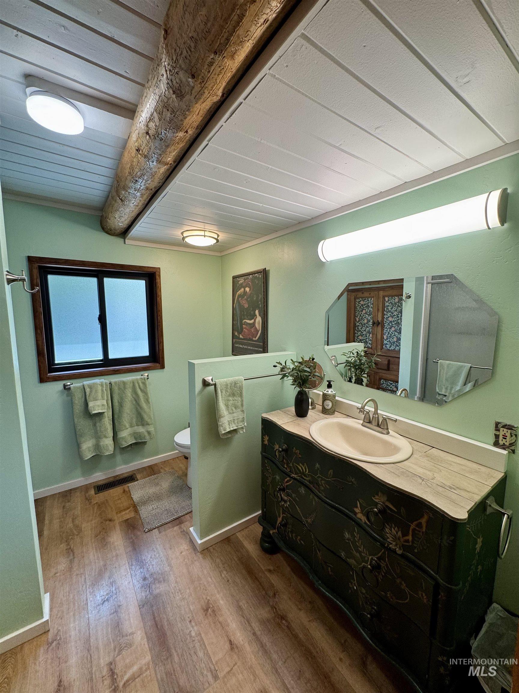 62 Bell Rapids Road Hagerman, ID 83332 - Photo 17 of 34 Bathroom featuring wood-finish flooring, a decorative vanity with an integrated sink, a rectangular mirror, a window with dark trim, and a white plank ceiling with an exposed wood beam