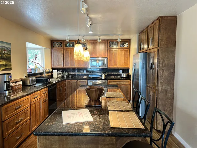 a kitchen with stainless steel appliances granite countertop a refrigerator a sink dishwasher a stove and white countertops with wooden floor