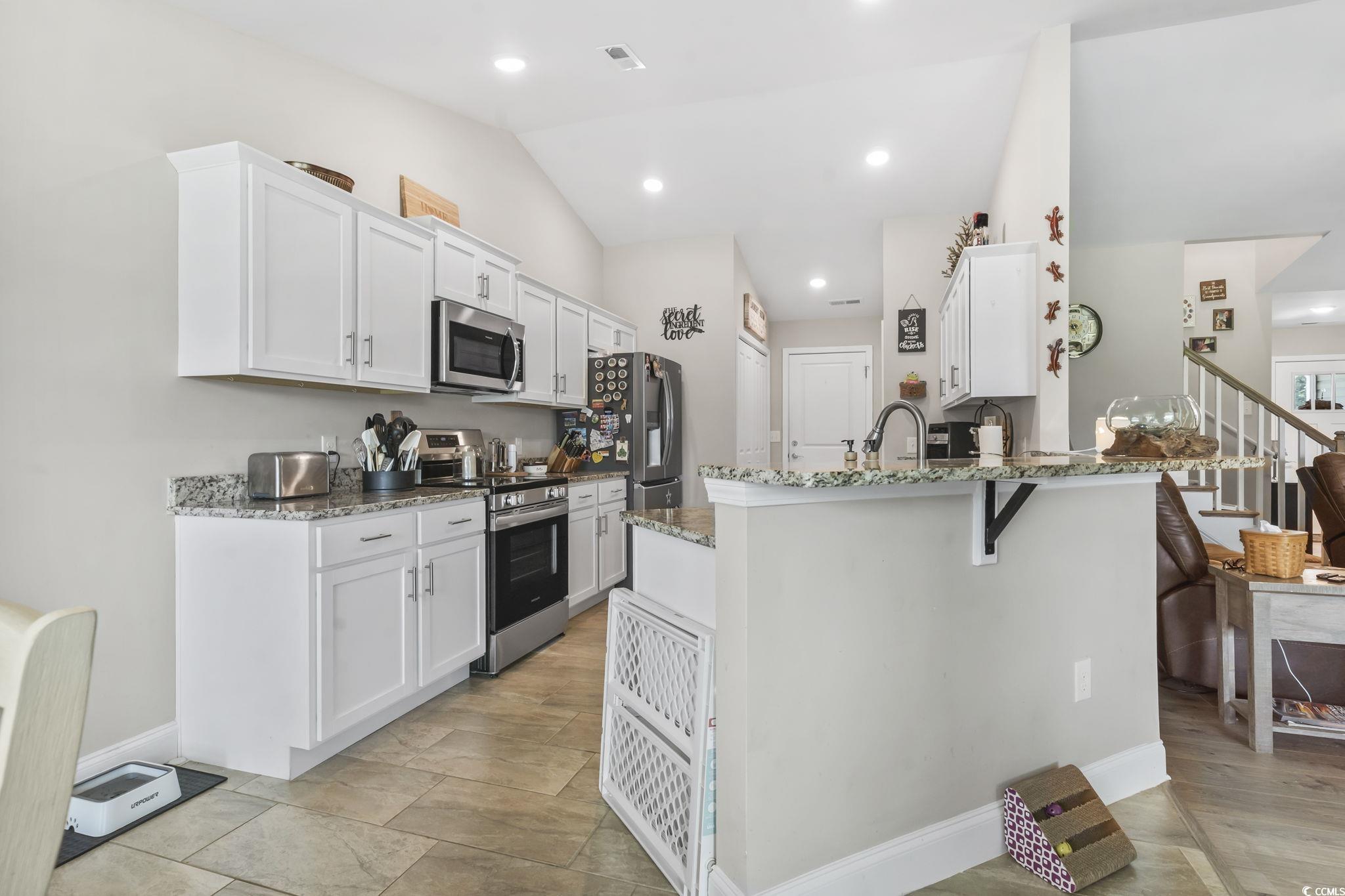 1170 Daisy Road Loris, SC 29569 - Photo 11 of 35 Kitchen with stainless steel appliances, lofted ceiling, light stone countertops, white cabinets, and a peninsula