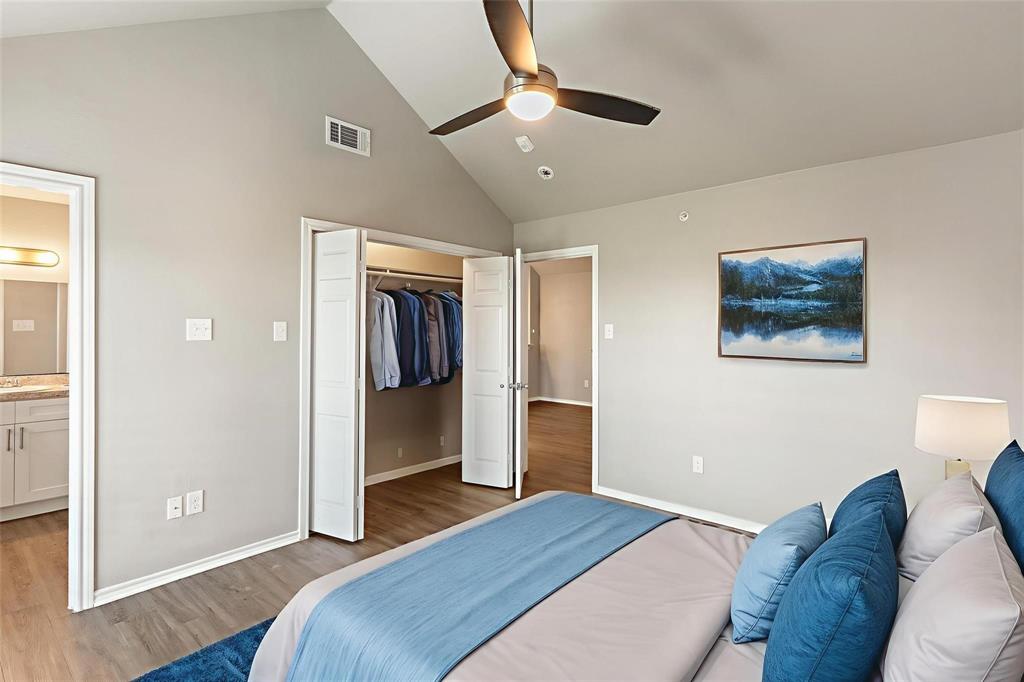 6108 Abrams Road, Unit 521 Dallas, TX 75231 - Photo 9 of 20 Bedroom featuring a vaulted ceiling with a flush-mount ceiling fan, wood-finish flooring, a bi-fold closet with interior shelving, and an entry to a bathroom with a vanity