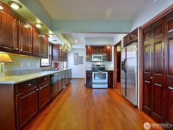 a kitchen with stainless steel appliances granite countertop a refrigerator a sink dishwasher a stove and wooden cabinets with wooden floor