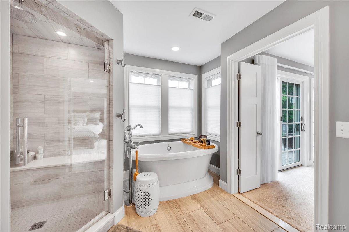 142 Griggs Street Rochester, MI 48307 - Photo 27 of 51 Spacious bathroom featuring a freestanding soaking tub, an expansive glass-enclosed shower with tile surround and bench, wood-finish flooring, and multiple windows