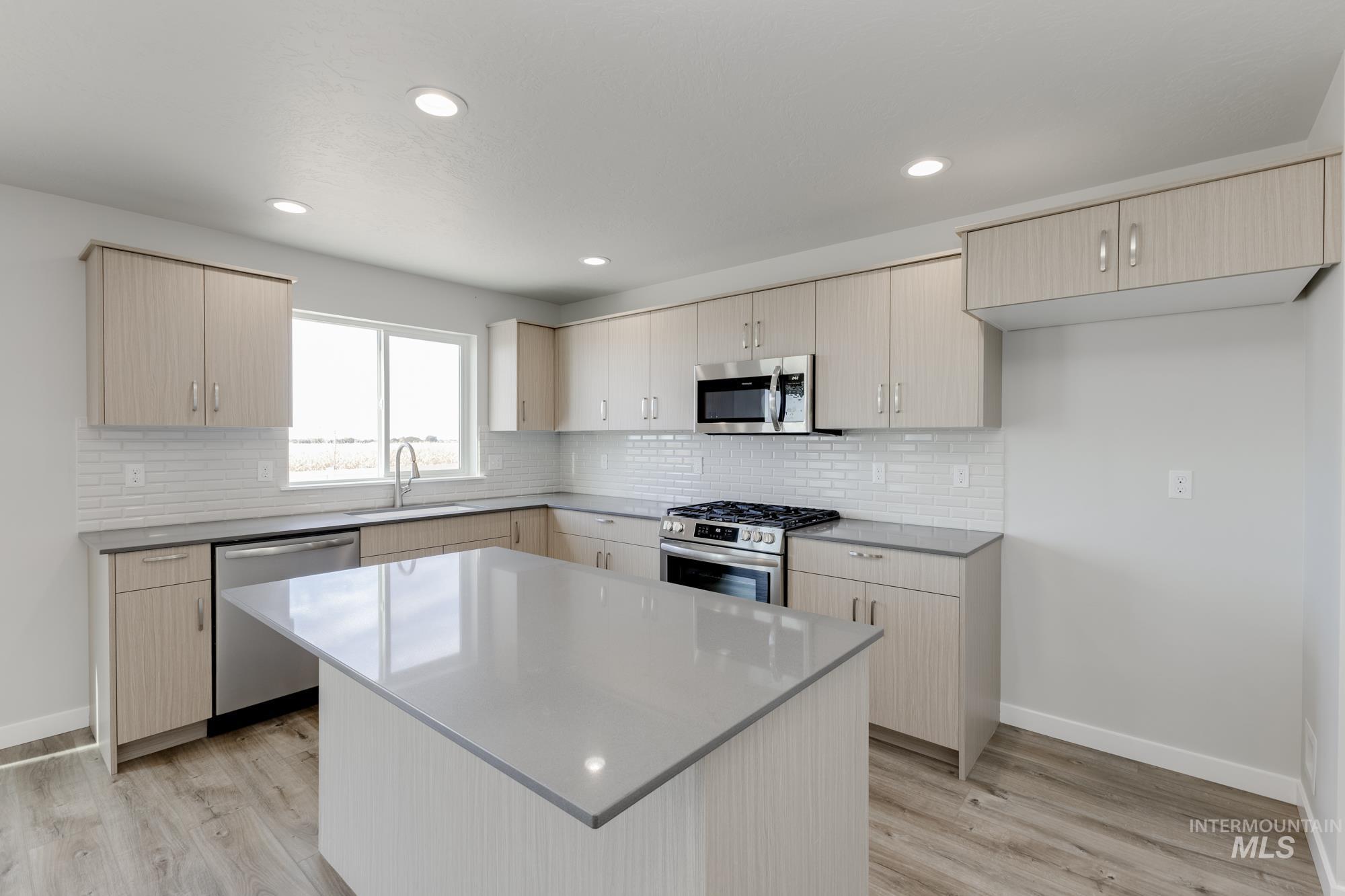 12853 Decatur Street Nampa, ID 83651 - Photo 3 of 24 Kitchen featuring an island with a light-toned countertop, wood-finish flooring, recessed lighting, stainless steel appliances, and a subway tile backsplash