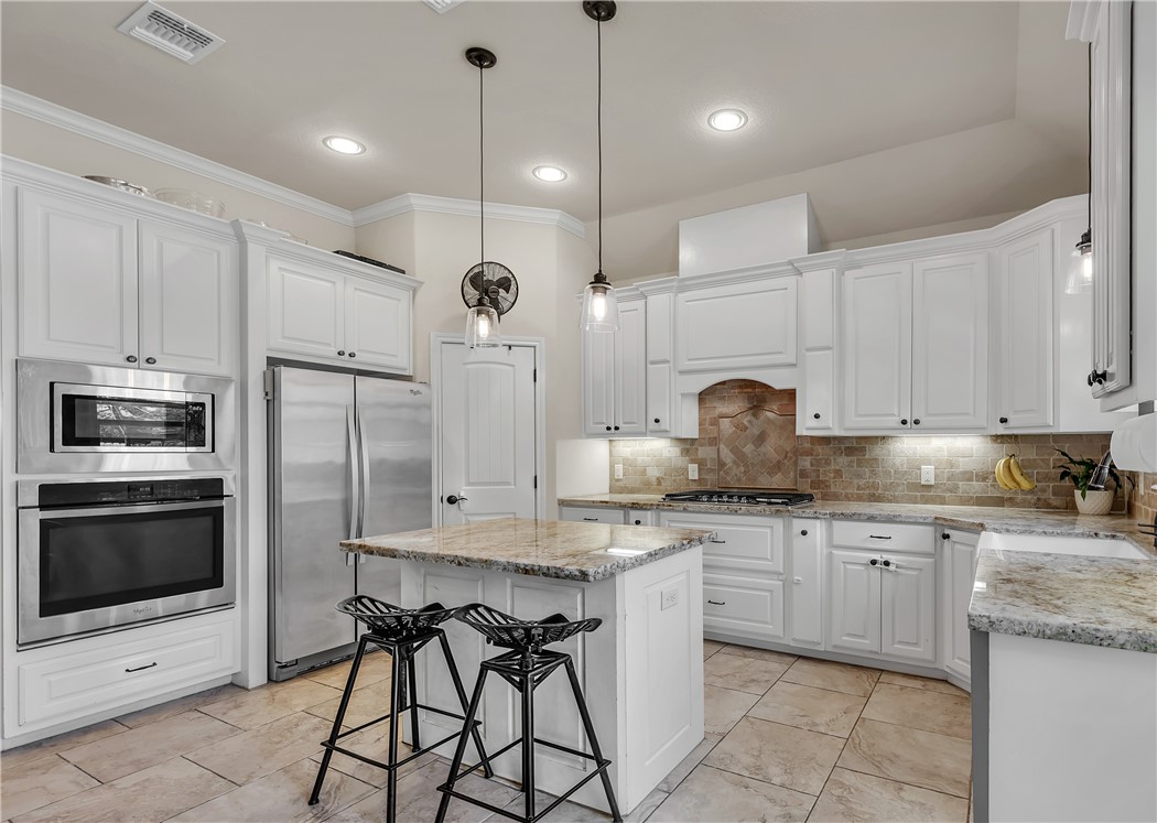 8312 Raintree Drive College Station, TX 77845 - Photo 10 of 30 Modern kitchen featuring white cabinetry, stainless steel appliances, a center island with pendant lighting, and stone countertops