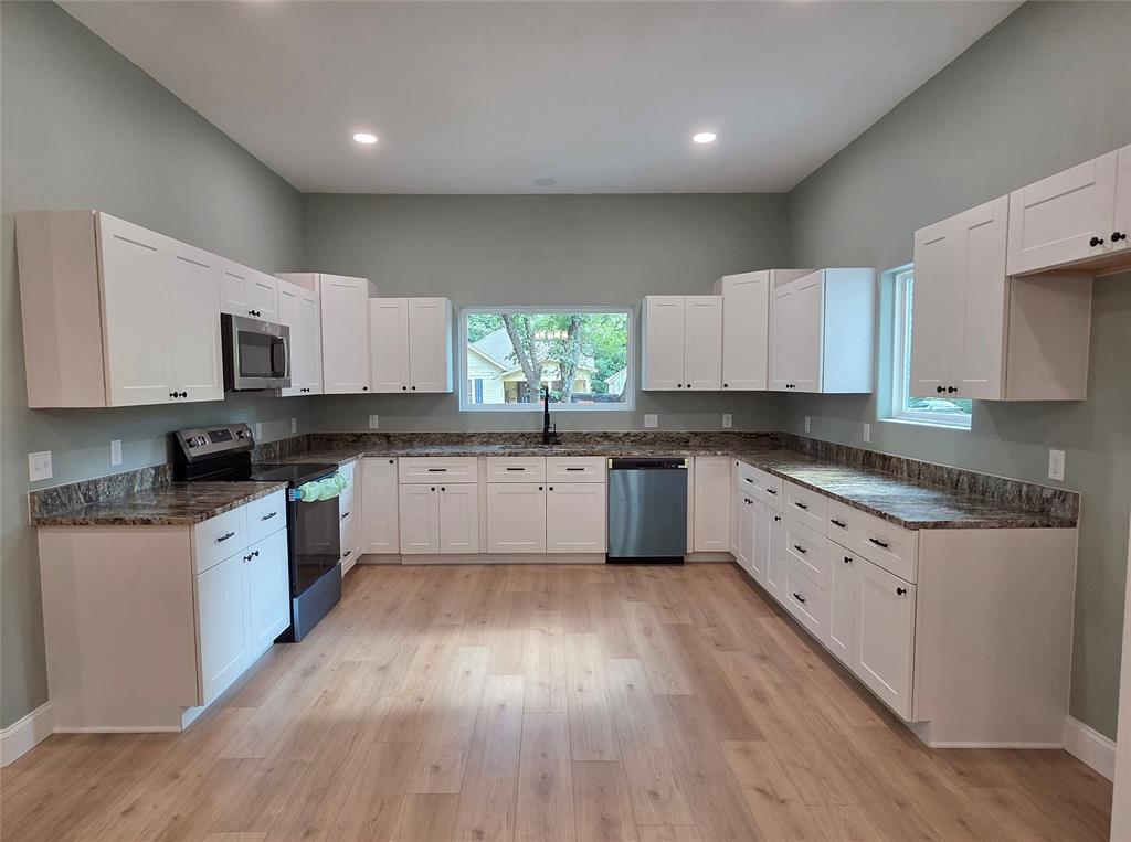 1745 East Cherry Street Paris, TX 75460 - Photo 7 of 40 a large kitchen with white cabinets a sink a window and stainless steel appliances