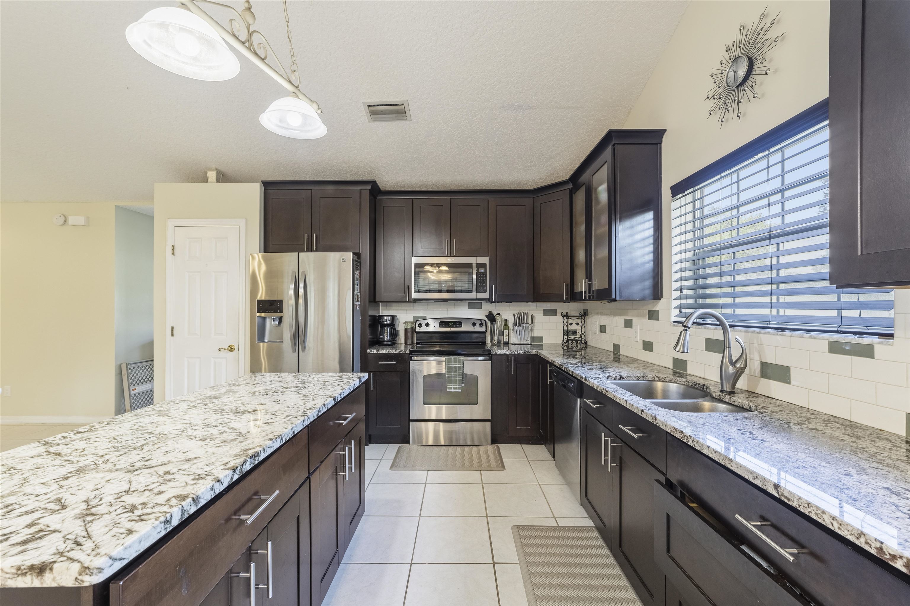 311 Graciela Circle St. Augustine, FL 32086 - Photo 13 of 65 Kitchen with appliances with stainless steel finishes, light stone counters, dark brown cabinetry, light tile patterned flooring, and hanging light fixtures