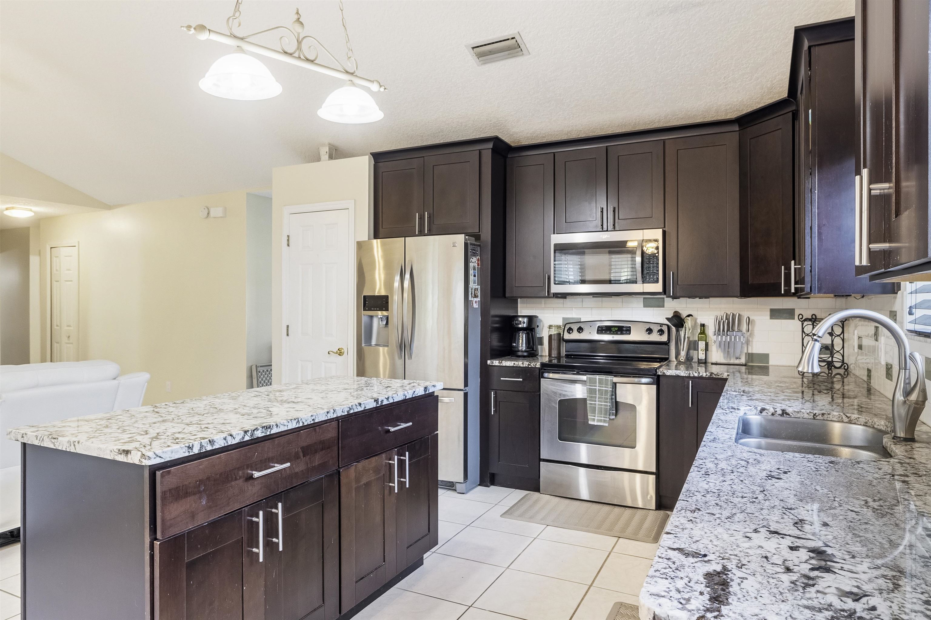 311 Graciela Circle St. Augustine, FL 32086 - Photo 16 of 65 Kitchen featuring dark brown cabinetry, appliances with stainless steel finishes, light tile patterned floors, a center island, and decorative backsplash