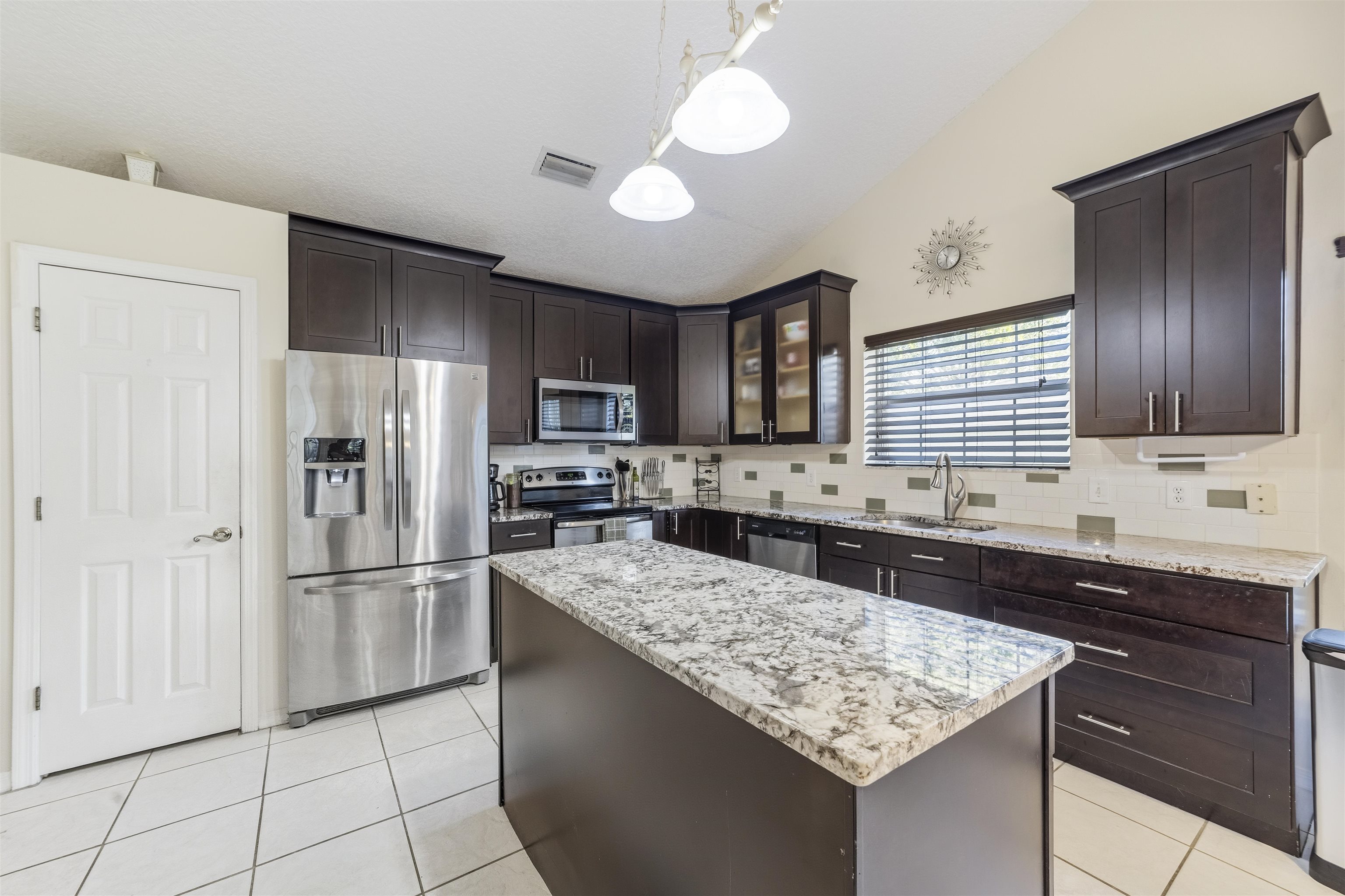 311 Graciela Circle St. Augustine, FL 32086 - Photo 17 of 65 Kitchen with dark brown cabinetry, appliances with stainless steel finishes, light tile patterned floors, a center island, and pendant lighting