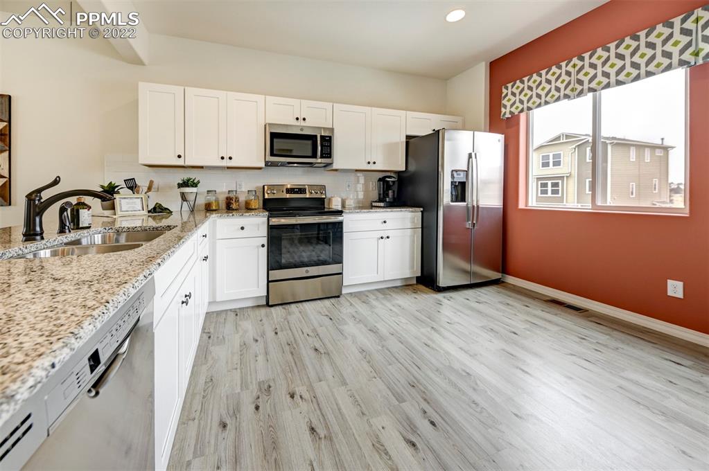 4456 Samaritan Loop Colorado Springs, CO 80916 - Photo 8 of 25 a large kitchen with stainless steel appliances granite countertop a stove a sink dishwasher and a refrigerator with wooden floor