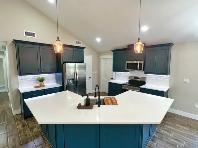 a kitchen with stainless steel appliances kitchen island granite countertop a sink a microwave a refrigerator and white cabinets with wooden floor