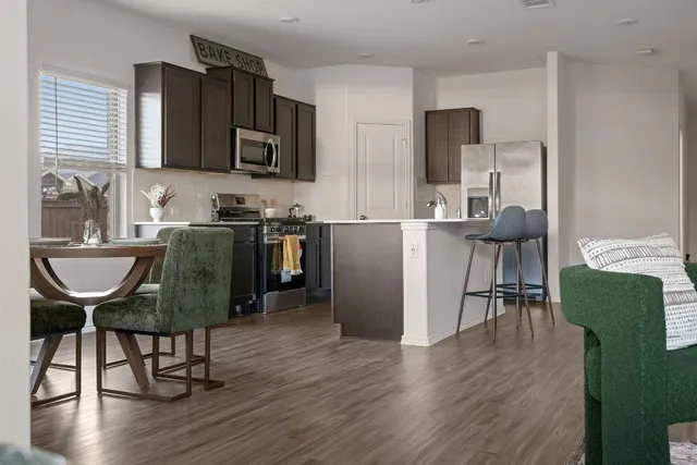 a kitchen with stainless steel appliances granite countertop a dining table chairs refrigerator and microwave