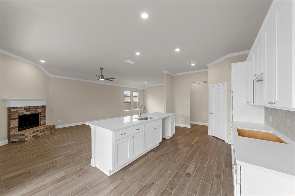 1508 Addison Lane Lancaster, TX 75134 - Photo 5 of 20 Open-concept living area featuring wood-finish flooring, a kitchen island with integrated sink, white cabinetry with stone countertops, a brick fireplace, and recessed lighting