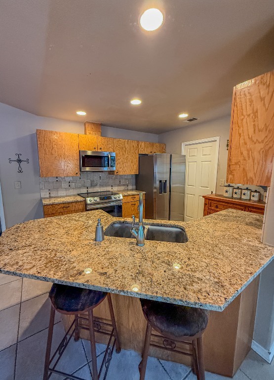 500 Jim Hogg Road Georgetown, TX 78633 - Photo 16 of 37 Kitchen featuring a kitchen bar, a peninsula, backsplash, appliances with stainless steel finishes, and brown cabinetry