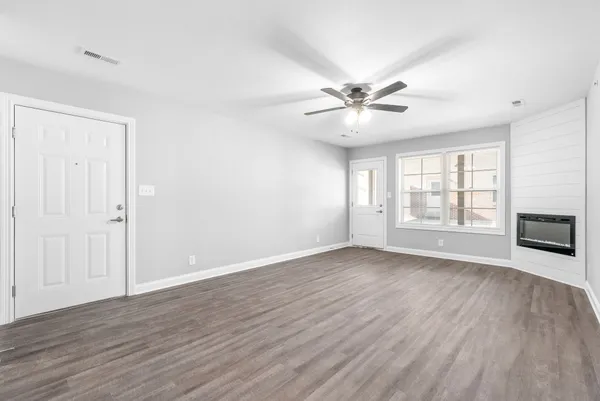 an empty room with wooden floor chandelier fan and windows