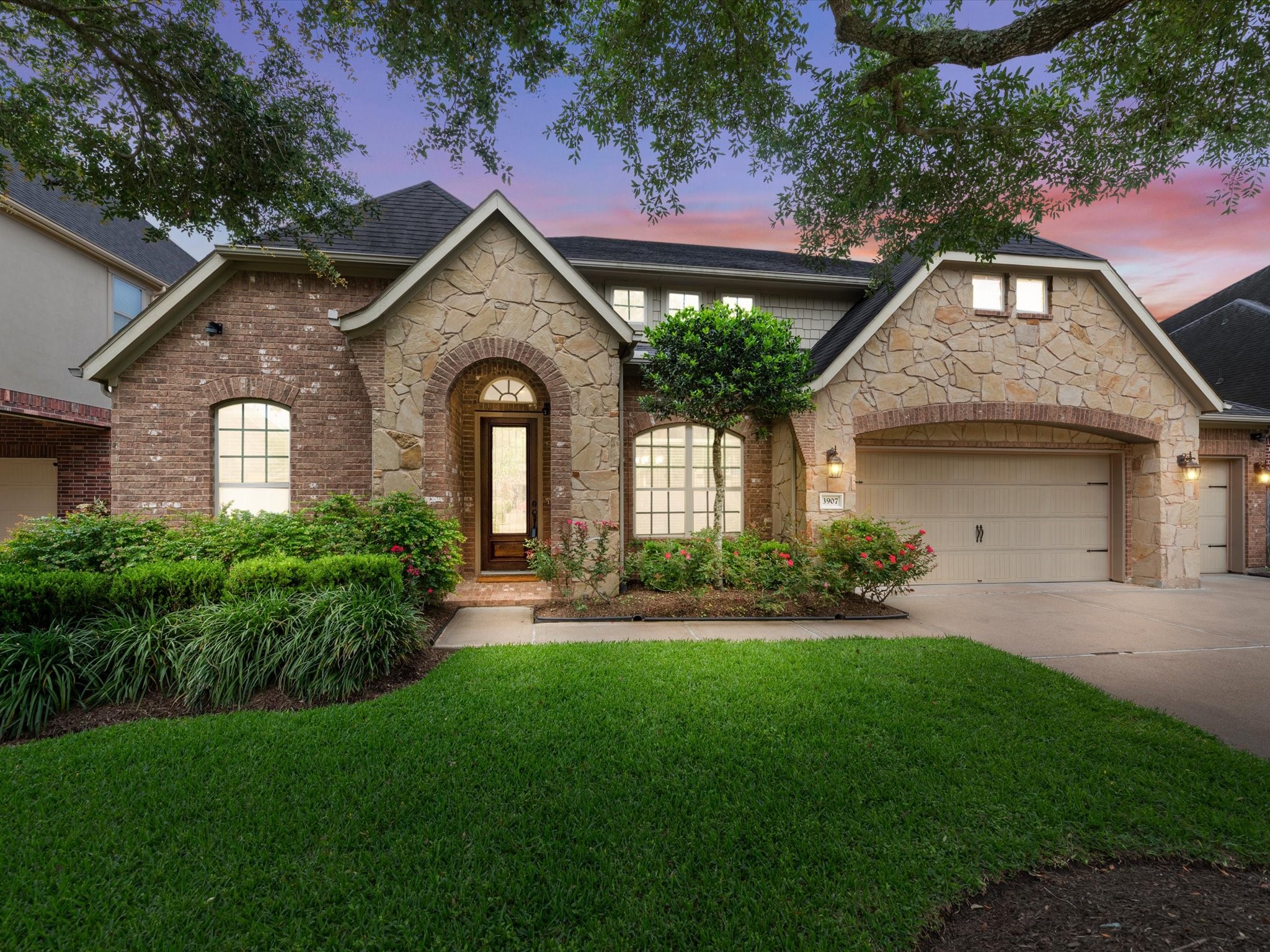 3907 Randle Ridge Court Fulshear, TX 77441 - Photo 2 of 46 This charming home features a beautiful stone and brick exterior with a well-manicured lawn and lush landscaping. The inviting entrance highlights a wooden front door, and the property includes a spacious driveway leading to a three-car garage. Perfect for those seeking a picturesque and welcoming residence. Virtually staged to be twilight.