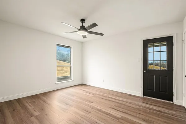 an empty room with wooden floor a ceiling fan and windows