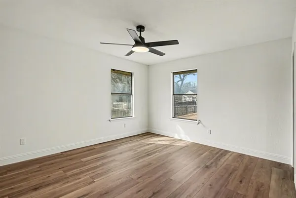an empty room with wooden floor ceiling fan and windows
