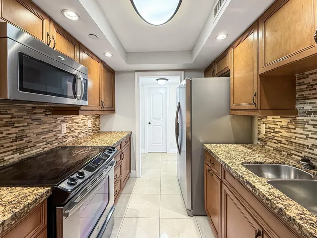 a kitchen with stainless steel appliances granite countertop a sink a stove a refrigerator a washer dryer and cabinets