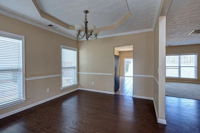 an empty room with wooden floor chandelier and windows