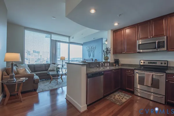 a kitchen with stainless steel appliances granite countertop a stove a sink dishwasher a microwave oven and a dining table with wooden cabinet