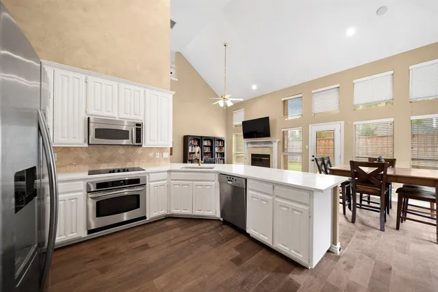 a kitchen with stainless steel appliances granite countertop a stove top oven a sink dishwasher a refrigerator and a dining table with wooden floor
