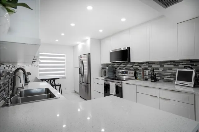 a kitchen with stainless steel appliances a sink a stove a microwave a refrigerator and cabinets