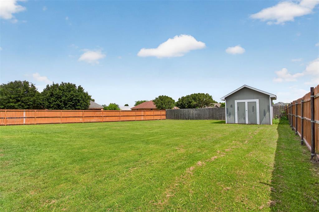 100 Radecke Road Krum, TX 76249 - Photo 29 of 29 Expansive green lawn featuring a privacy fence, a detached storage shed, and mature perimeter trees
