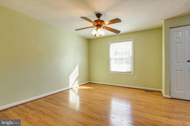 an empty room with wooden floor fan and windows