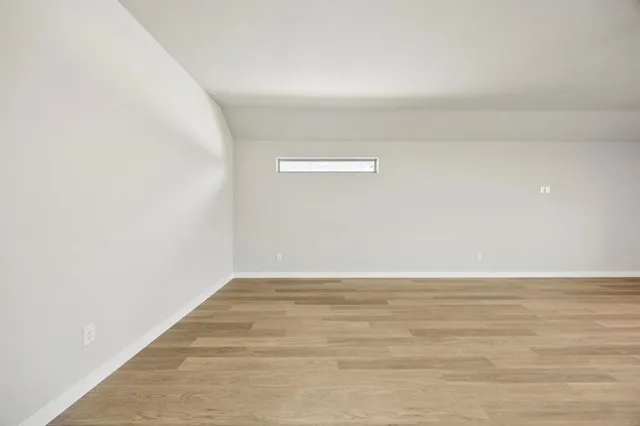 a view of an empty room and kitchen view and wooden floor