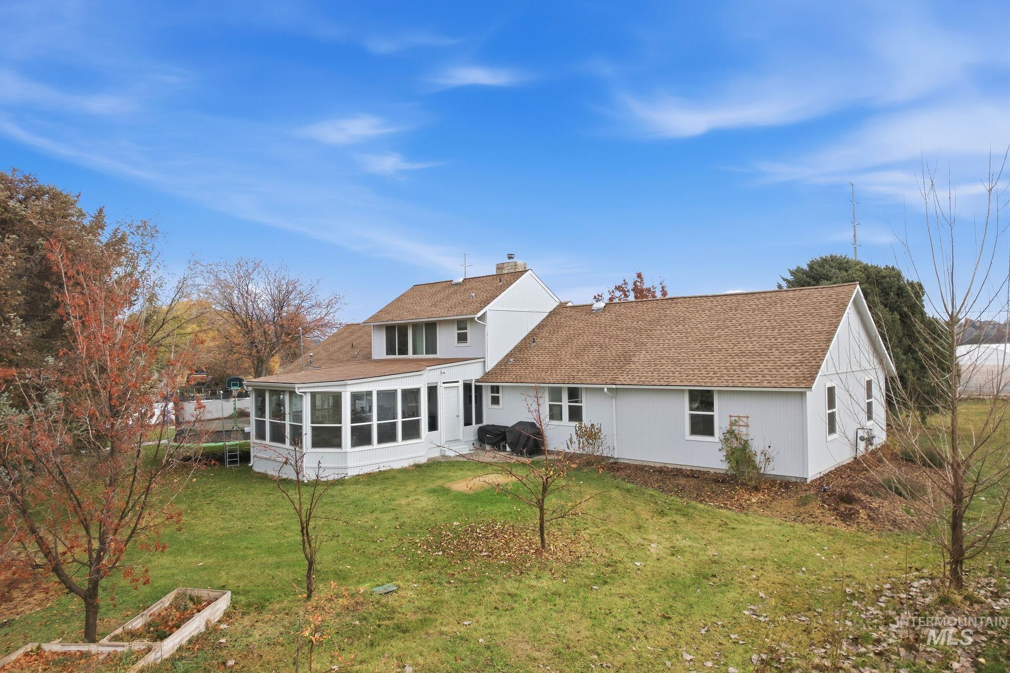 7985 South Cloverdale Road Boise, ID 83709 - Photo 34 of 49 Rear view of property featuring a sunroom, a yard, a shingled roof, and a chimney