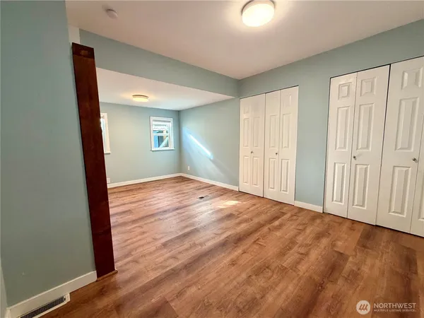 an empty room with wooden floor closet and windows