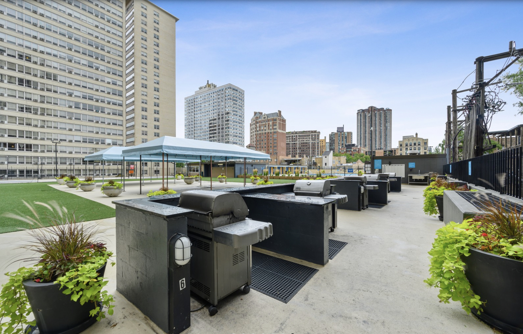 655 West Irving Park Road, Unit 1006 Chicago, IL 60613 - Photo 20 of 22 a view of a patio with table and chairs under an umbrella with a barbeque grill and potted plants