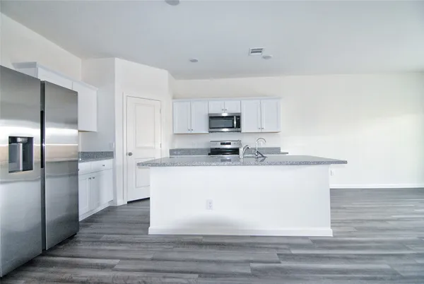 a large white kitchen with kitchen island a sink wooden floor and stainless steel appliances