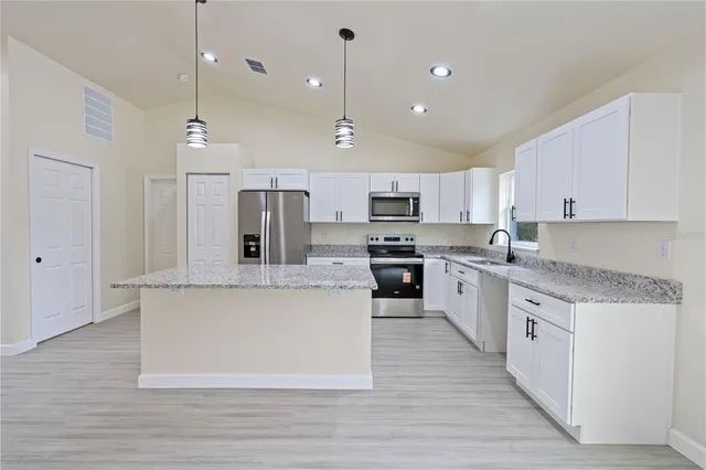 a large kitchen with stainless steel appliances kitchen island a stove a sink dishwasher a refrigerator and white cabinets with wooden floor