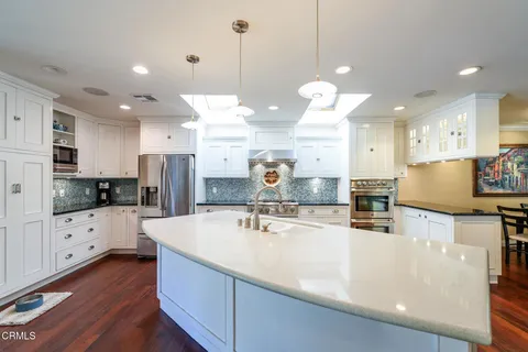 a kitchen with stainless steel appliances kitchen island granite countertop a refrigerator a stove a sink and white cabinets with wooden floor