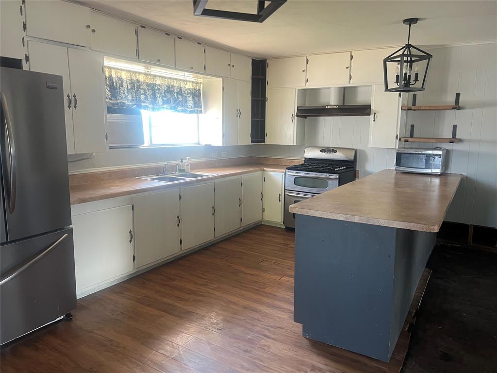 203 Washington Avenue Strawn, TX 76475 - Photo 5 of 20 Kitchen with decorative light fixtures, appliances with stainless steel finishes, dark wood-style flooring, a peninsula, and white cabinetry