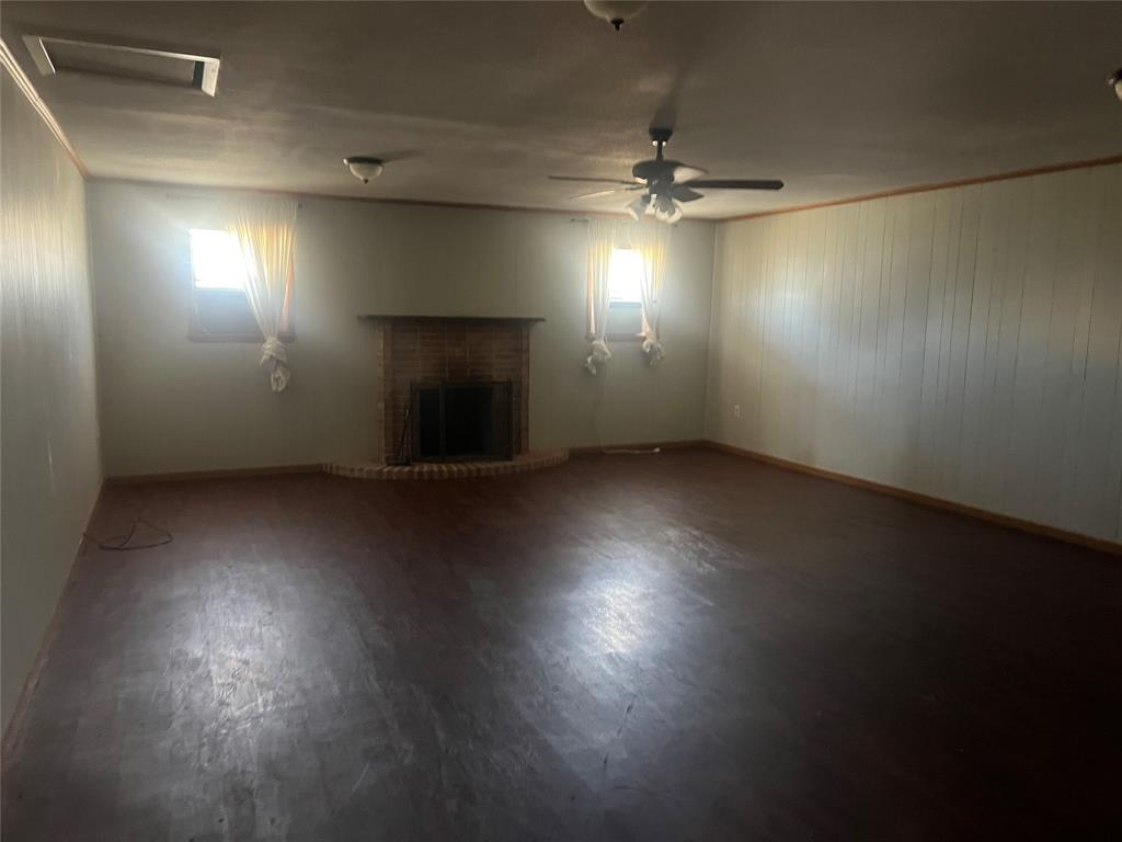 203 Washington Avenue Strawn, TX 76475 - Photo 9 of 20 Unfurnished living room featuring ornamental molding, wood finished floors, a fireplace, and wooden walls