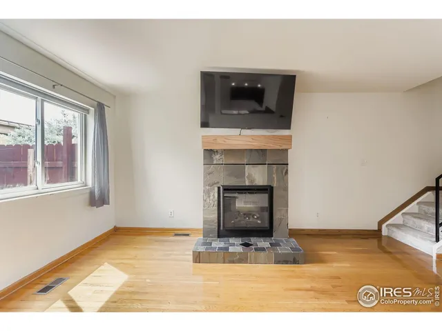 a view of an empty room with wooden floor fireplace and a window