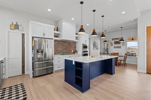 a kitchen with stainless steel appliances kitchen island granite countertop a refrigerator a stove and a wooden floors