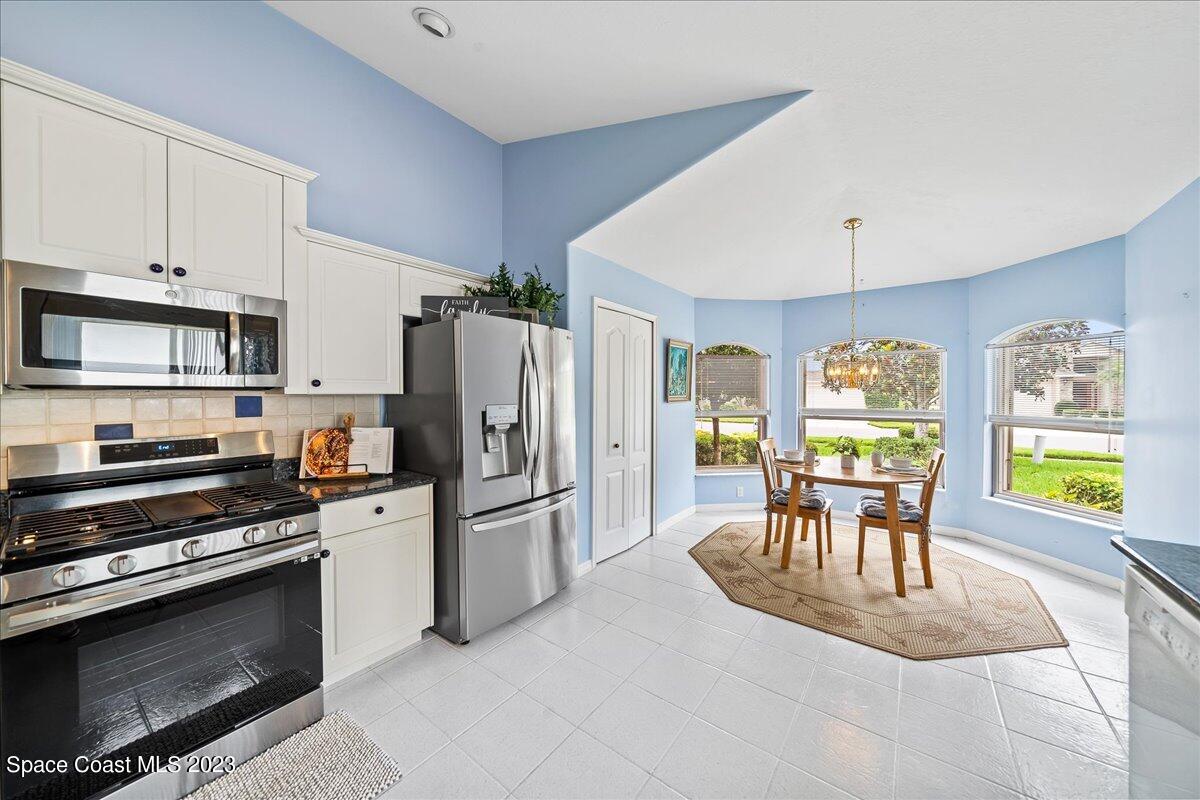 1643 Keys Gate Drive Melbourne, FL 32940 - Photo 13 of 43 a kitchen with stainless steel appliances kitchen island granite countertop a refrigerator a stove a microwave a dining table and chairs with wooden floor