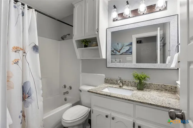 a bathroom with a granite countertop sink a toilet a mirror a vanity and shower