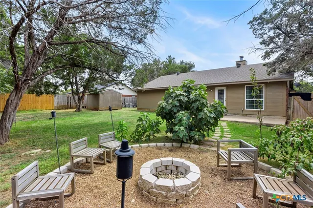 a view of a backyard with table and chairs potted plants and large tree